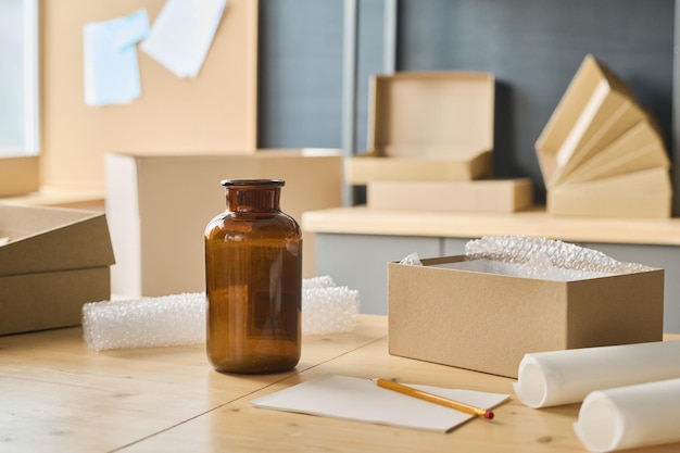 Closeup of workplace with glass bottle standing on it and
opened cardboard boxes for packing parcels