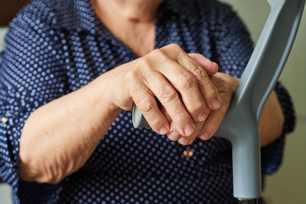 Primo piano delle mani rugose di una donna pensionata con una stampella