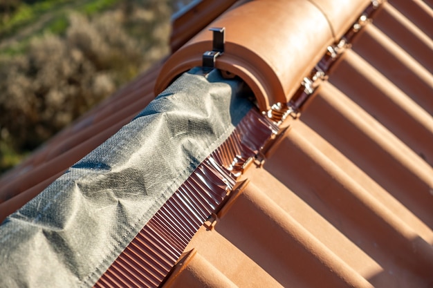 Photo closeup of yellow ceramic roofing ridge tiles on top of residential building roof under construction.