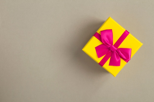 Closeup on yellow gift box with pink ribbon on the gray 