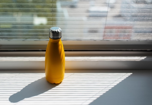 Closeup of yellow metal thermo water bottle on window sill