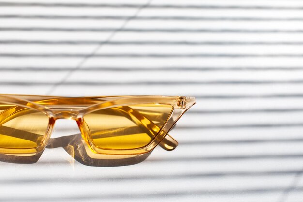 Closeup of yellow transparent sunglasses on white striped background by shadows