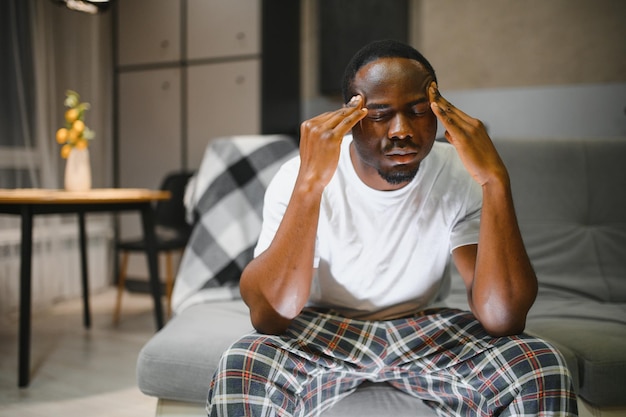 closeup of young african american man suffering from headache at home touching his temples migraine headache stress tension problem hangover concept