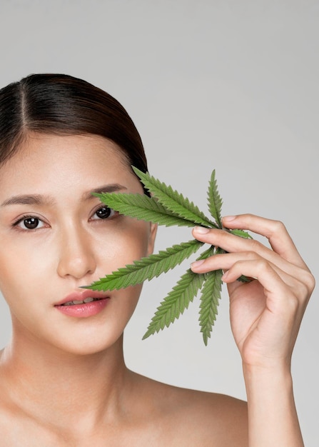 Closeup young ardent girl with healthy fresh skin holding green hemp leaf