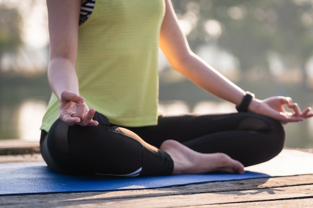 Primo piano di una giovane bella donna asiatica che pratica yoga e medita nella posa del loto all'aperto accanto al lago al mattino per il relax e la pace della mente. armonia e concetto di meditazione.