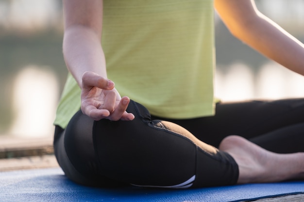 Closeup of a young Asian beautiful woman practicing yoga and meditate in the lotus pose outdoor beside the lake in the morning for relaxation and peace of mind. Harmony and meditation concept.