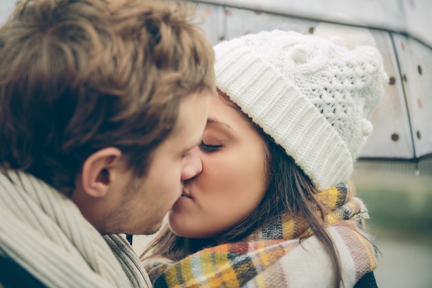 秋の雨の日に傘の下でキスする若い美しいカップルのクローズアップ。愛とカップルの関係の概念。