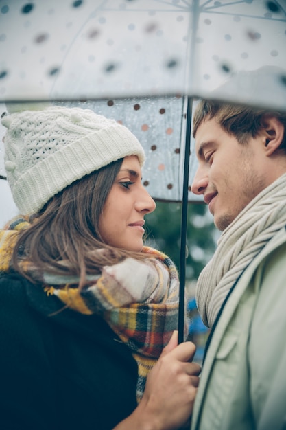 秋の雨の日に傘の下で愛を込めてお互いを見ている若い美しいカップルのクローズアップ。愛とカップルの関係の概念。