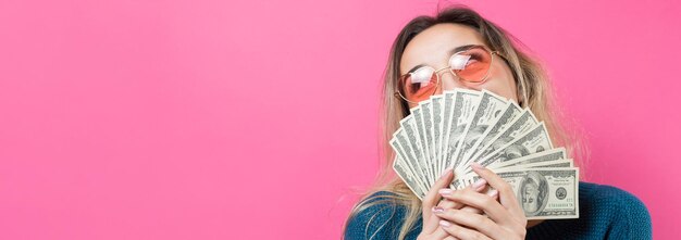 アメリカのドルのお金と旗とメガネの青いセーターの若い美しい女性のクローズアップ