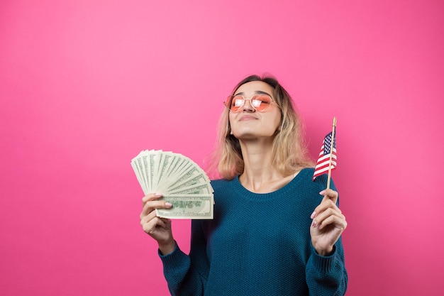 Closeup of young beautiful woman in a blue sweater in glasses with american dollars money and flag