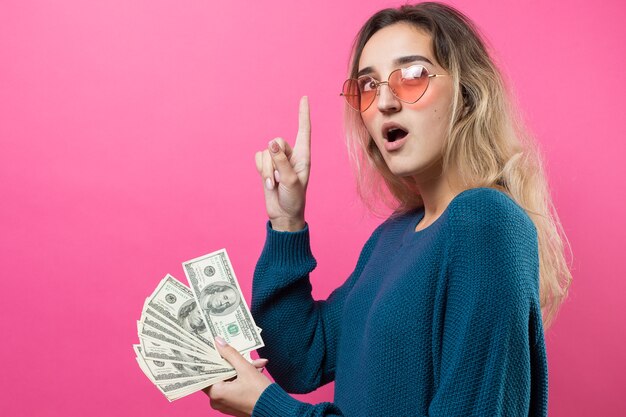 Closeup of young beautiful woman in a blue sweater in glasses with american dollars money in hand