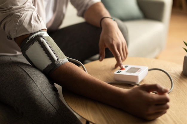 Closeup of young black man checking blood pressure using modern tonometer at home