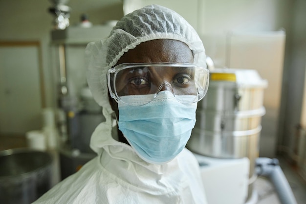 Closeup young black man wearing mask and protective suit working at factory