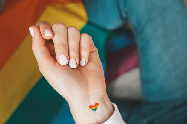 Photo closeup of young caucasian millennial hippie woman with a rainbow flag in heart shape painted