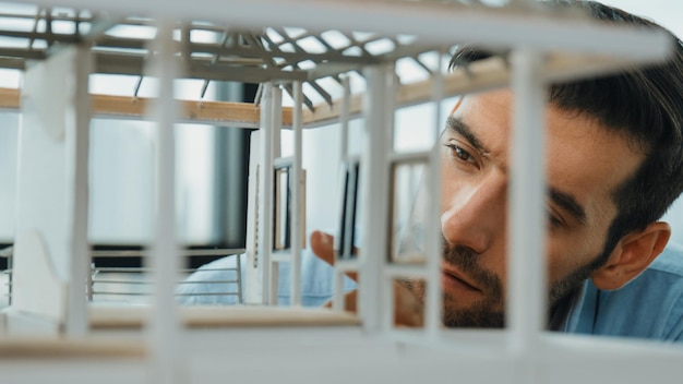 Foto close-up di un giovane ingegnere architetto caucasico qualificato che si concentra sul controllo della struttura del modello di casa con fiducia un operaio maschile che guarda la costruzione della casa concetto di progettazione creativa tracery