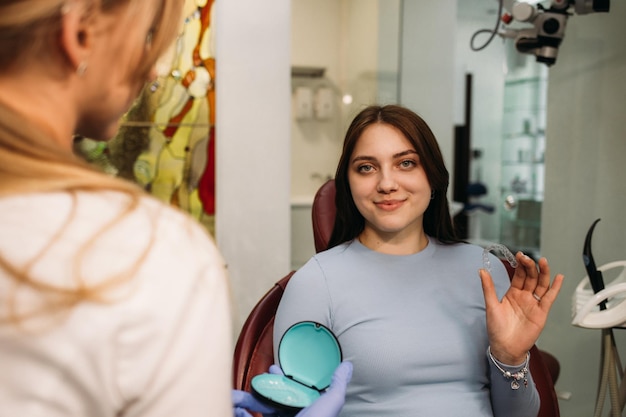 Крупный план молодой кавказской женщины, держащей невидимый элайнер, который она хочет надеть на зубы Концепция лечения зубов