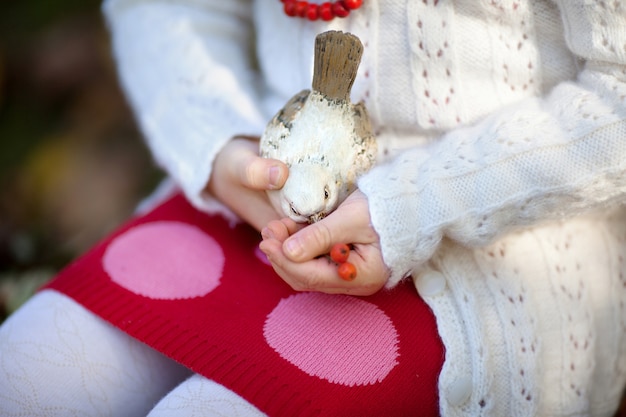 Closeup young child small hands holding creative ceramic handmade crafts black white bird.  Little girl feeding your ceramic bird with mountain ash berries.  Unique gift for friend friends or family