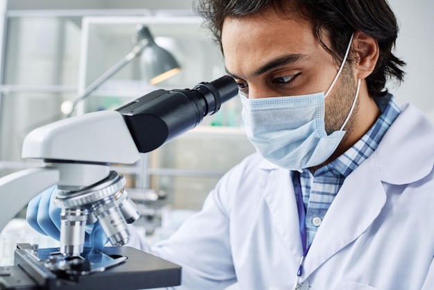 Foto primo piano di un giovane medico in maschera protettiva che studia nuovi virus o batteri