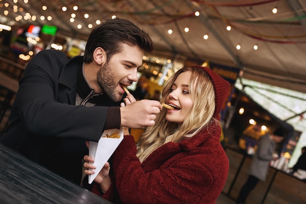 Closeup of young couple are eating french fries at the street food market