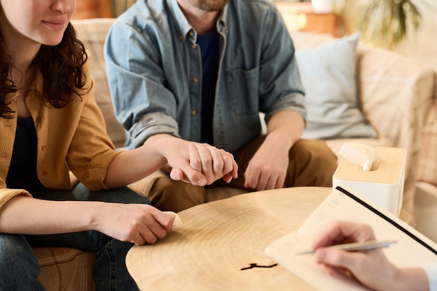 Closeup of young couple holding hands and supporting each other while visiting psychologist