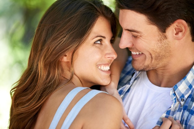 Closeup of a young couple loving in the park and standing in the summer sun under the tree Cheerful bonding outdoor and romantic partners affectionate and playful smiling on vacation in nature