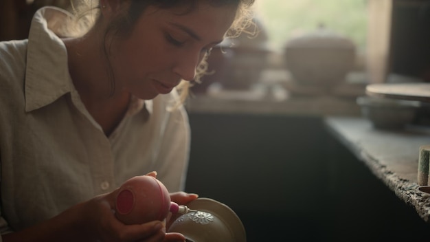 Closeup young craftmaster making decoration in studio Portrait of beautiful woman drawing ornament in workshop Excited female artist doing handicraft on clay product in pottery