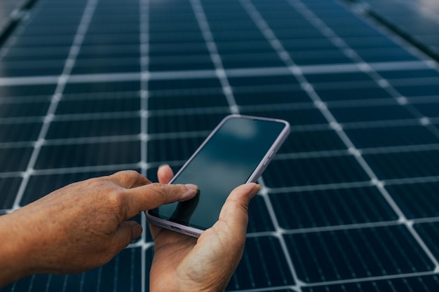 Крупный план молодого инженера, держащего смартфон на фоне панели в солнечный день, концепция зеленой альтернативной энергии, высококачественное фото