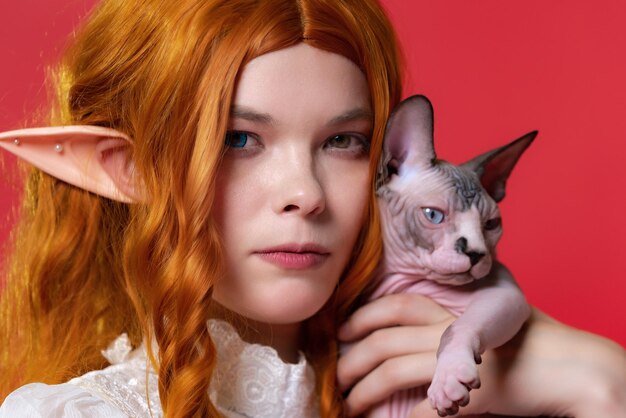 Closeup of young female elf cosplay with curly red hair looking at camera hugging Sphinx cat