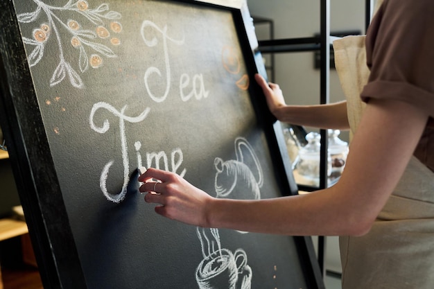 Closeup of young female worker of cafe drawing letters with chalk