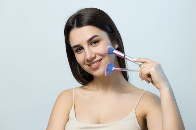 Closeup of a young girl in a light top on a white background making a facial makeup