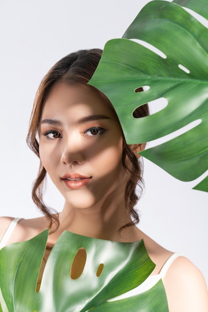 Closeup young gorgeous woman with healthy skin holding green leaf near her face