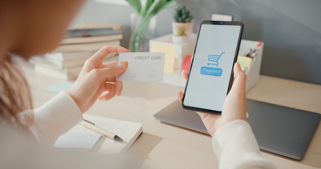 Closeup young lady use cellphone order online shopping product and pay bills with credit card in living room interior at house, 