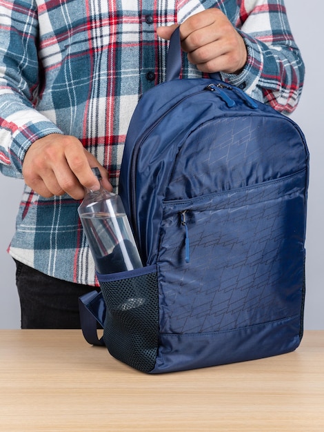 Foto primo piano di un giovane studente maschio che tira fuori una bottiglia d'acqua dal suo zaino