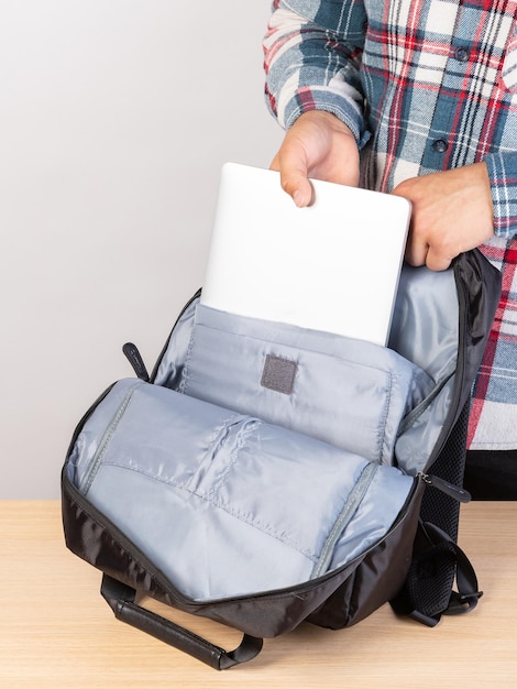 Foto primo piano di un giovane studente maschio che tira fuori un computer portatile da uno zaino