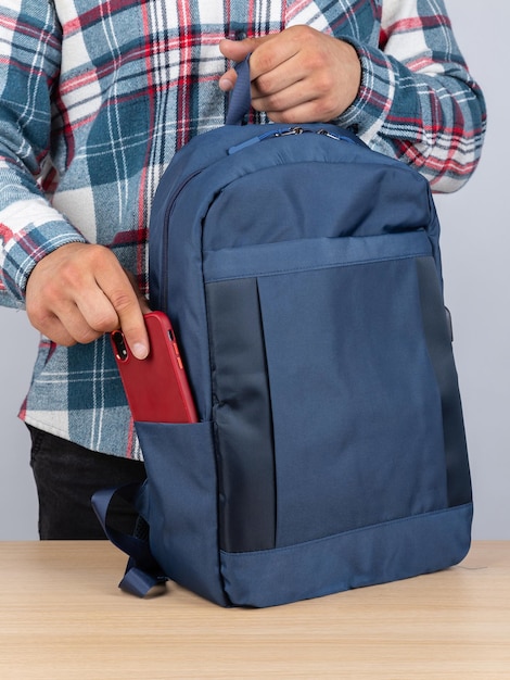 Closeup of a young male student taking out a phone from his backpack