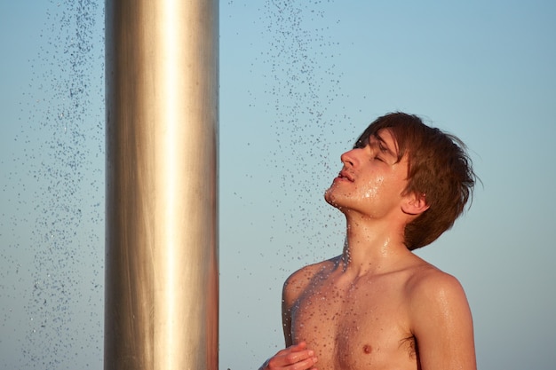 A closeup of the young man taking a shower on the beach.