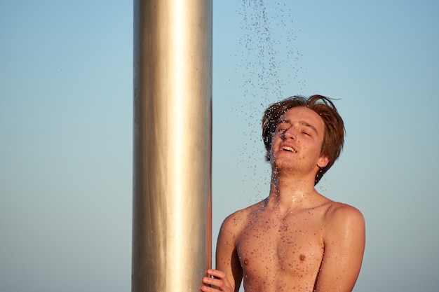 A closeup of the young man taking a shower on the beach.