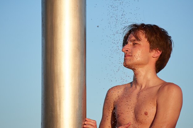 A closeup of the young man taking a shower on the beach.