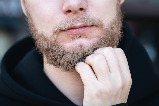 Closeup a young man touches his beard with his hand