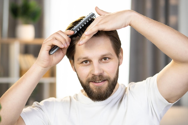 Closeup of a young positive caucasian guy in a white tshirt combing his hair