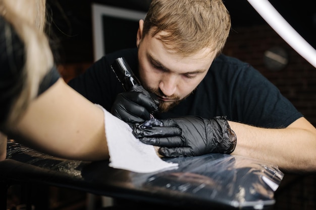 Крупный план молодого профессионального художника-татуировщика вводит в кожу черные чернила с помощью иглы из