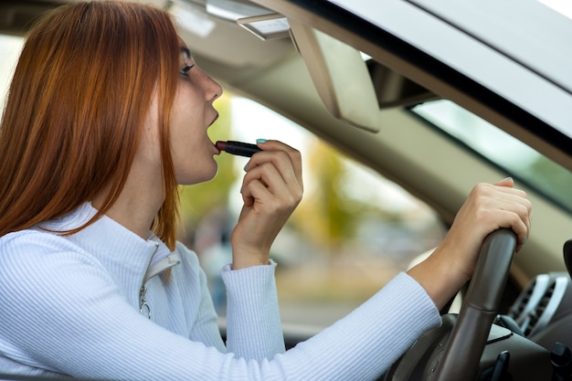 Closeup of a young redhead woman driver correcting her makeup