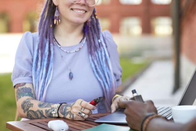 Closeup of young smiling businesswoman with vape pen networking at meeting