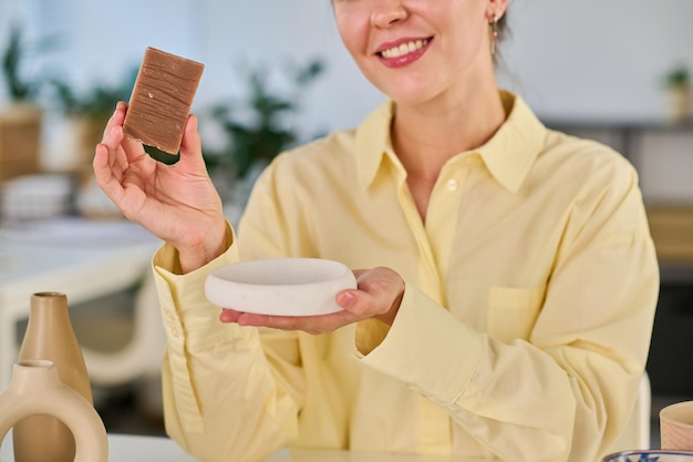 Closeup of young smiling female holding bar of handmade soap and describing its characteristics to online audience during livestream