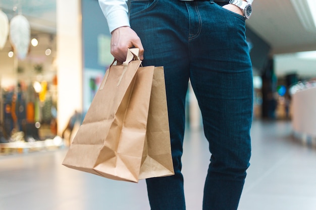 エコロジーにやさしい買い物袋を手に商品や服を持ってモールを歩いている若いスタイリッシュな男のクローズアップ。販売、割引完売コンセプト。季節限定完売。