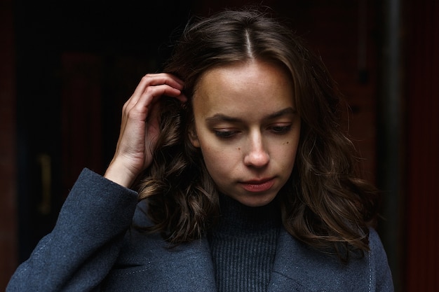 Closeup on young thoughtful pretty girl in gray coat and turtleneck posing outdoors