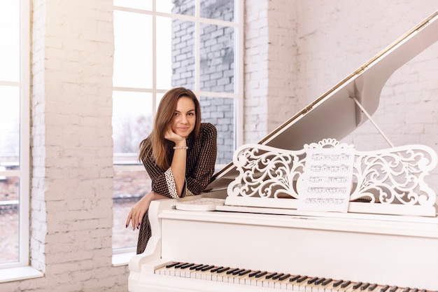 Closeup of a young woman in a brown dress leaning on a piano