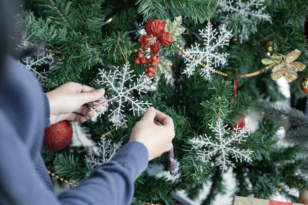 クリスマスのお祝いのクリスマスツリーを飾る若い女性の後ろのクローズアップ。新年を祝います。メリークリスマスと幸せな休日。