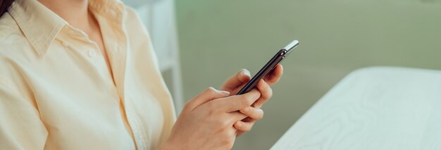 スマートフォンを押しながらソーシャルネットワークで友達とチャットする若い女性の手のクローズアップ。