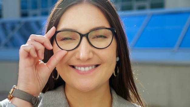 Closeup of a young woman straightening glasses and smiling at the camera